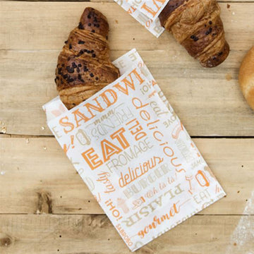 sacchetto alimentare di carta con scritte arancioni con dentro un cornetto al cioccolato su tavola di legno